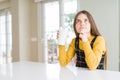 Beautiful young girl driking a glass of fresh milk serious face thinking about question, very confused idea Royalty Free Stock Photo