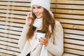 Beautiful young girl drinking coffee, tea from plastic mug in autumn, winter and talking on mobile phone. Woman with long hair Royalty Free Stock Photo