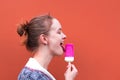 Beautiful and young girl eats a pink hue ice cream and enjoys. She closed her eyes from pleasure and licked his tongue.