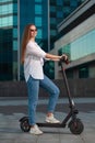 Beautiful young girl is enjoying sunny summer day while riding around the city on electro kick scooters. Lifestyle. Royalty Free Stock Photo