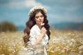 Beautiful young girl with flower enjoying in chamomile field. Carefree happy brunette woman with chaplet on healthy wavy hair