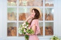 Beautiful young girl in a gently pink dress, holding a bouquet of roses in one hand. Happy woman holding a straw hat on the backgr Royalty Free Stock Photo