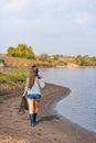 A beautiful young girl goes fishing. A girl with a fishing rod and a cage in hand is walking along the lake Royalty Free Stock Photo