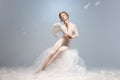 Beautiful young girl, graceful ballerina in image of angel with wings sitting on cloud isolated on white gray studio Royalty Free Stock Photo