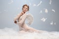 Beautiful young girl, graceful ballerina in image of angel with wings sitting on cloud  on white gray studio Royalty Free Stock Photo