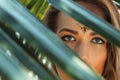 Beautiful young girl with grey eyes and bindi behind palm leaves.