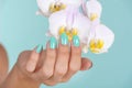 Graceful Hand with Turquoise Manicure and Delicate Lilac Orchid Flower