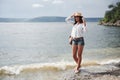 A beautiful young girl in a hat and with a backpack playfully walks by the water. A warm summer day is a great time for Royalty Free Stock Photo
