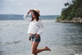 A beautiful young girl in a hat and with a backpack playfully walks by the water. A warm summer day is a great time for Royalty Free Stock Photo