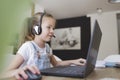 Beautiful young girl with headset is sitting in front of her laptop during corona time and is having video call Royalty Free Stock Photo