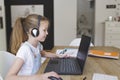 Beautiful young girl with headset is sitting in front of her laptop during corona time and is having video call Royalty Free Stock Photo