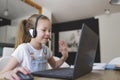 Beautiful young girl with headset is sitting in front of her laptop during corona time and is having video call Royalty Free Stock Photo