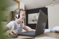 Beautiful young girl with headset is sitting in front of her laptop during corona time and is having video call Royalty Free Stock Photo