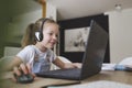 Beautiful young girl with headset is sitting in front of her laptop during corona time and is having video call Royalty Free Stock Photo