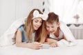 A beautiful young girl and her cheerful younger brother look at photos on their phone while lying on the bed with a smile. Brother