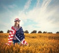 Beautiful young girl holding an American flag in a field of wheat. Summer landscape against the blue sky Royalty Free Stock Photo