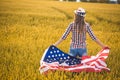 Beautiful young girl holding an American flag in a field of wheat. Summer landscape against the blue sky Royalty Free Stock Photo