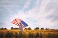 Beautiful young girl holding an American flag on the wind in a field of wheat. Summer landscape against the blue sky Royalty Free Stock Photo