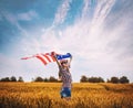 Beautiful young girl holding an American flag on the wind in a field of wheat. Summer landscape against the blue sky Royalty Free Stock Photo