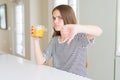 Beautiful young girl kid drinking a glass of fresh orange juice with angry face, negative sign showing dislike with thumbs down, Royalty Free Stock Photo