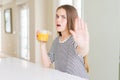 Beautiful young girl kid drinking a glass of fresh orange juice with open hand doing stop sign with serious and confident Royalty Free Stock Photo