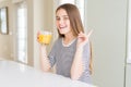 Beautiful young girl kid drinking a glass of fresh orange juice very happy pointing with hand and finger to the side Royalty Free Stock Photo