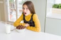 Beautiful young girl kid eating chocolate cereals and glass of milk for breakfast afraid and shocked with surprise expression, Royalty Free Stock Photo