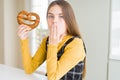 Beautiful young girl kid eating german snack salty pretzel cover mouth with hand shocked with shame for mistake, expression of