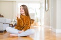 Beautiful young girl kid sitting on the floor at home smiling with happy face looking and pointing to the side with thumb up Royalty Free Stock Photo