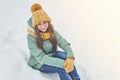 A beautiful young girl in a knitted hat sits on the snow Royalty Free Stock Photo