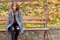 Beautiful young girl with large autumn sad eyes in a coat and ripped black jeans sitting on a bench in autumn park Royalty Free Stock Photo