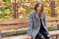 Beautiful young girl with large autumn sad eyes in a coat and ripped black jeans sitting on a bench in autumn park Royalty Free Stock Photo