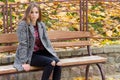 Beautiful young girl with large autumn sad eyes in a coat and ripped black jeans sitting on a bench in autumn park Royalty Free Stock Photo