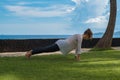 Beautiful young girl in leggings and tunic makes yoga practice, meditation, plank asana on the ocean beach Bali Indonesia Royalty Free Stock Photo