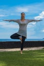 Beautiful young girl in leggings and tunic makes yoga practice, meditation, standing asana on the ocean beach Bali Indonesia Royalty Free Stock Photo