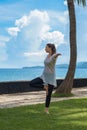 Beautiful young girl in leggings and tunic makes yoga practice, meditation, stranding asana on the ocean beach Bali Indonesia Royalty Free Stock Photo