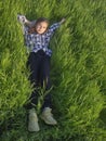 A beautiful young girl lies in the green grass under the sun. A happy girl enjoys life on a lush lawn and looks up at the sky