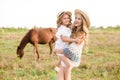 A beautiful young girl, with light curly hair in a straw hat with a little sister hugging and laughing near horses Royalty Free Stock Photo