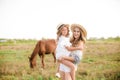 A beautiful young girl, with light curly hair in a straw hat with a little sister hugging and laughing near horses Royalty Free Stock Photo