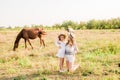 A beautiful young girl, with light curly hair in a straw hat with a little sister hugging and laughing near horses Royalty Free Stock Photo