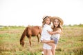 A beautiful young girl, with light curly hair in a straw hat with a little sister hugging and laughing near horses Royalty Free Stock Photo