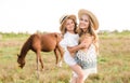 A beautiful young girl, with light curly hair in a straw hat with a little sister hugging and laughing near horses Royalty Free Stock Photo