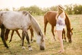 A beautiful young girl, with light curly hair in a straw hat near horses, in the countryside, warm autumn Royalty Free Stock Photo