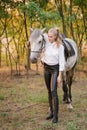 Beautiful young girl with light hair in uniform competition hugs her horse : outdoors portrait on sunny day on sunset Royalty Free Stock Photo