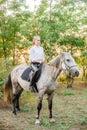 Beautiful young girl with light hair in uniform competition smiling and astride a horse in sunset