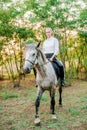 Beautiful young girl with light hair in uniform competition smiling and astride a horse in sunset