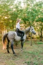 Beautiful young girl with light hair in uniform competition smiling and astride a horse in sunset