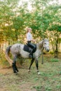 Beautiful young girl with light hair in uniform competition smiling and astride a horse in sunset