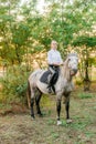 Beautiful young girl with light hair in uniform competition smiling and astride a horse in sunset