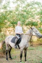 Beautiful young girl with light hair in uniform competition smiling and astride a horse in sunset